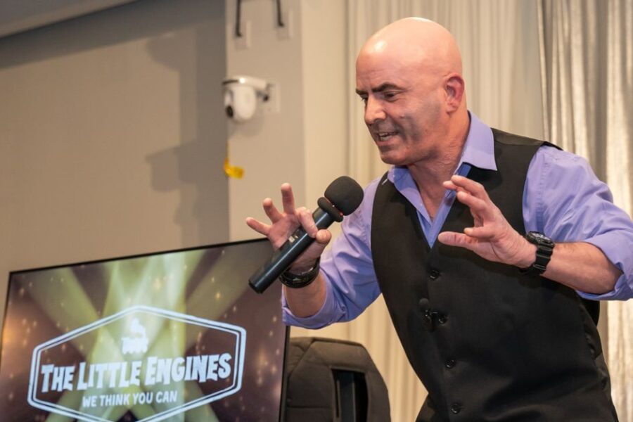 Keynote speaker Kevin Bulmer on stage at a Little Engines live event in a powerful stance, illustrating resilience by pushing back against opposing forces.