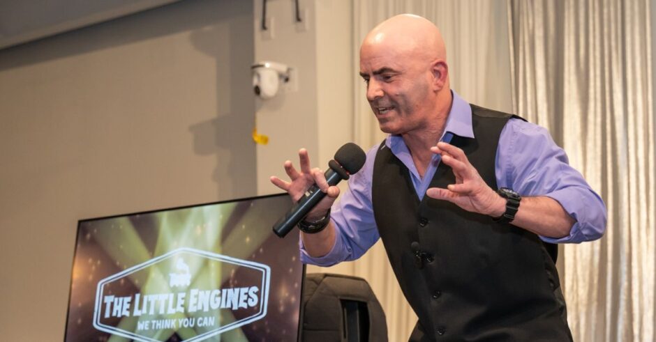 Keynote speaker Kevin Bulmer on stage at a Little Engines live event in a powerful stance, illustrating resilience by pushing back against opposing forces.