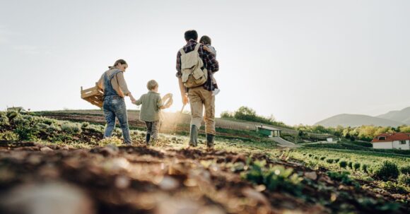 A family spending time together in a grassy field on a sunny summer day, surrounded by nature on a farm with no animals visible, enjoying each other's company.