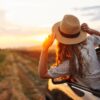 Young woman with her head out the car window, riding into a golden sunset — a visual blend of restful escape and adventurous freedom.