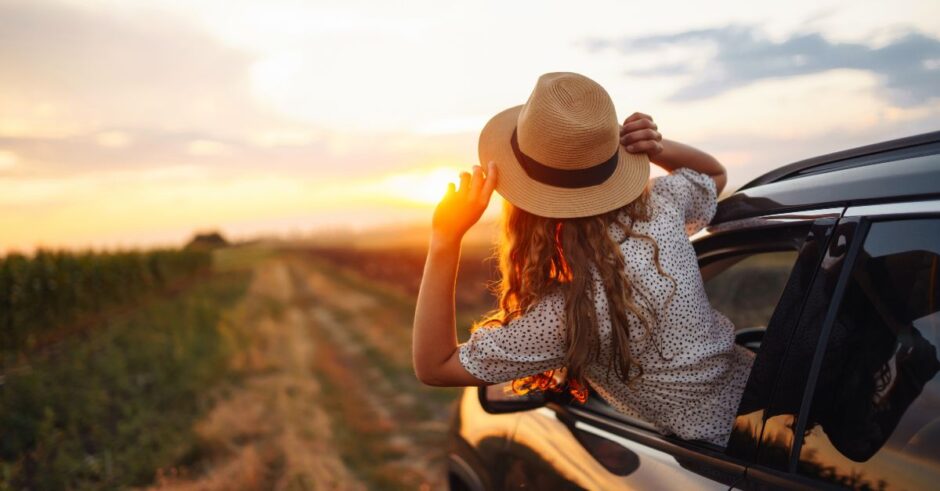 Young woman with her head out the car window, riding into a golden sunset — a visual blend of restful escape and adventurous freedom.